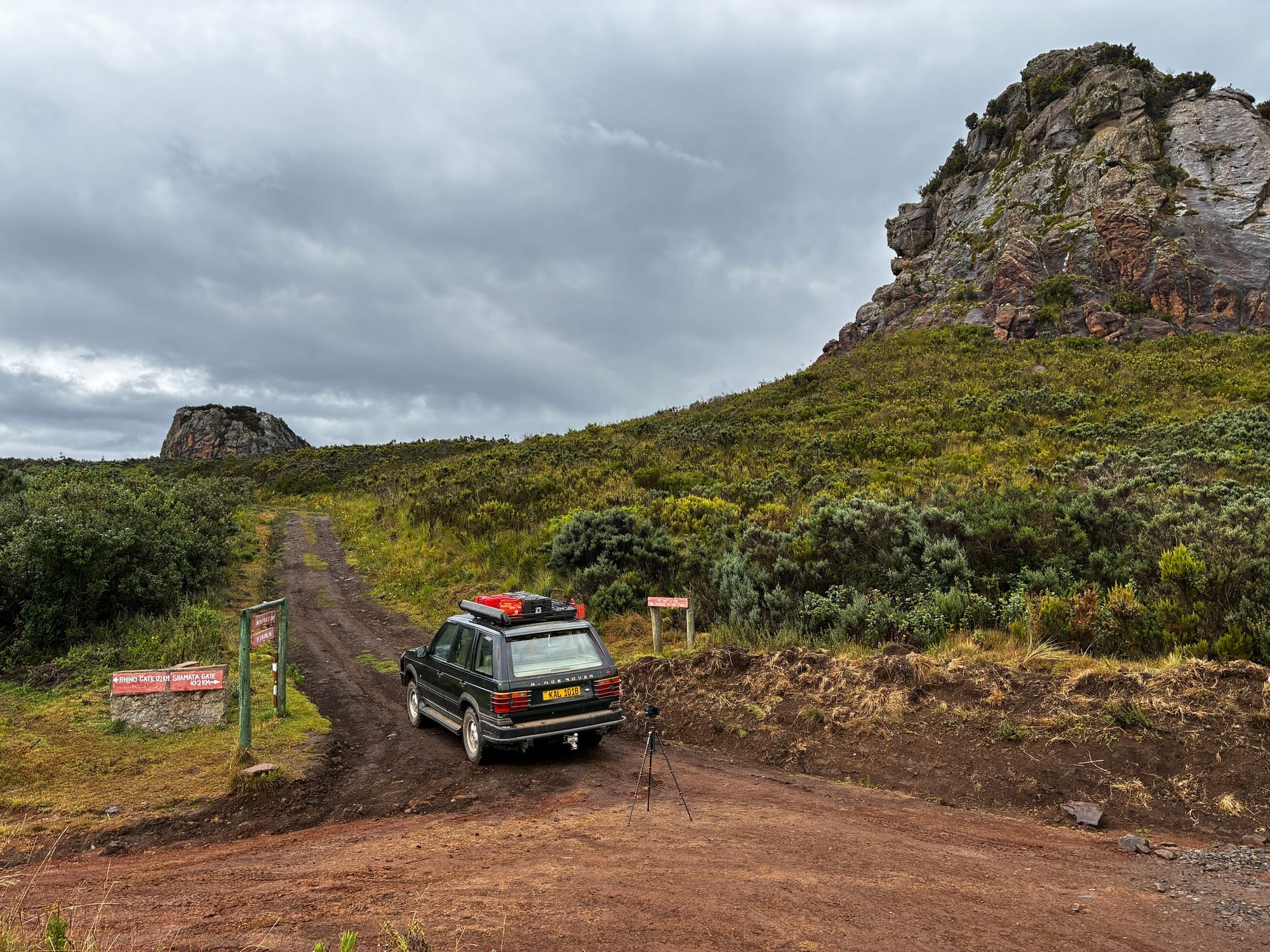 A vehicle is parked beside trail signs beneath the rock outcrops at Twin Rocks.